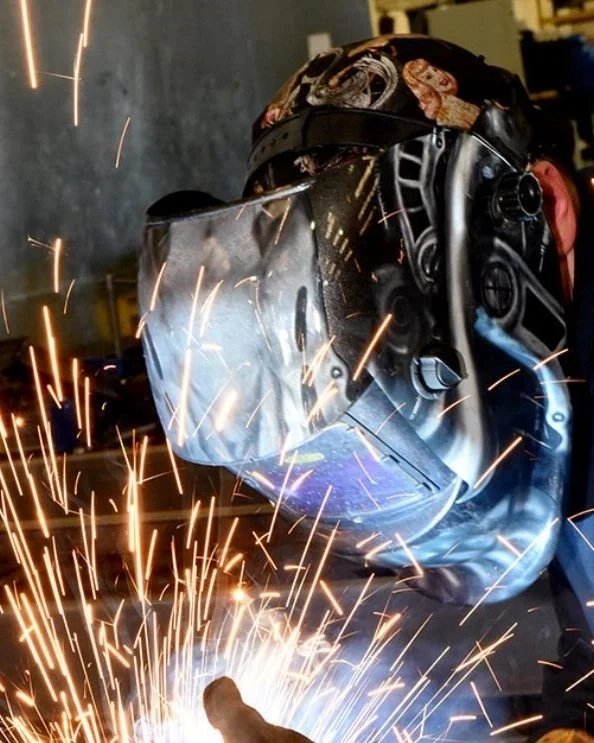 We Are Gateway engineer in a protective mask creating sparks while working on metal.